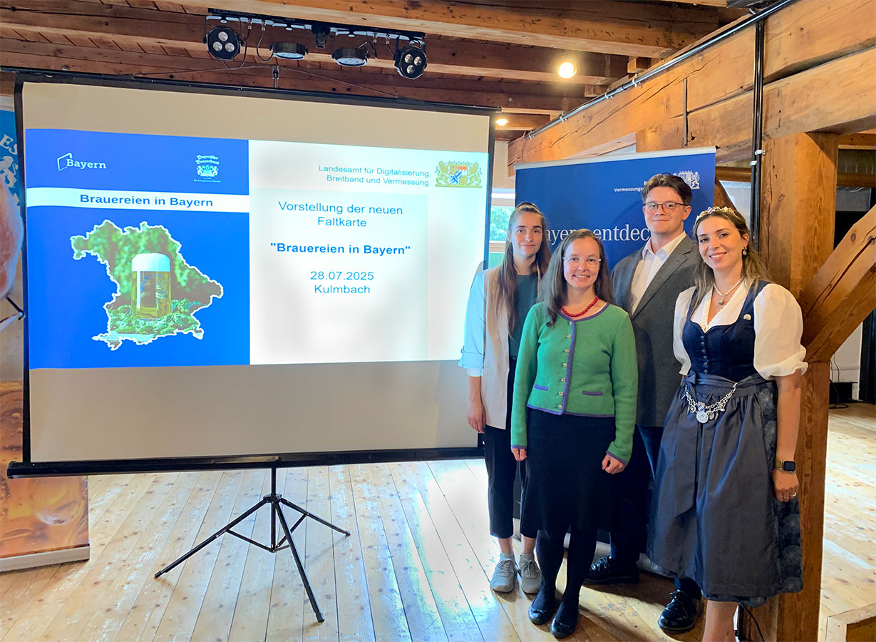 Neuauflage der Sonderkarte "Brauereien in Bayern"  Vier Personen stehen für ein Gruppenbild neben der Präsentationsleinwand aufgereiht